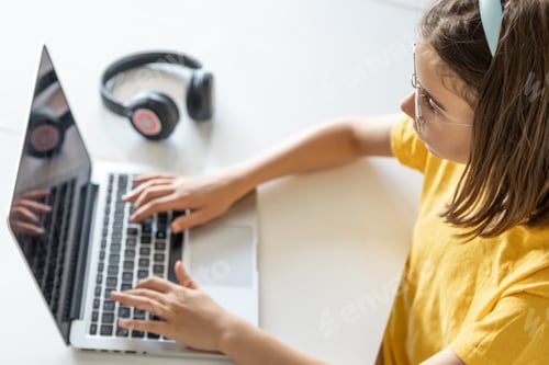Preview: A teenage girl in glasses uses a laptop while sitting at a table at home.
