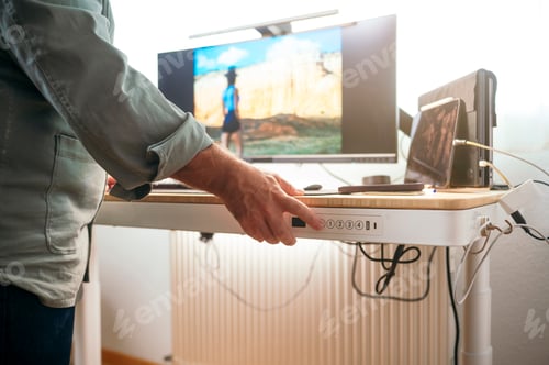Preview: Man raising standing desk in bright office.
