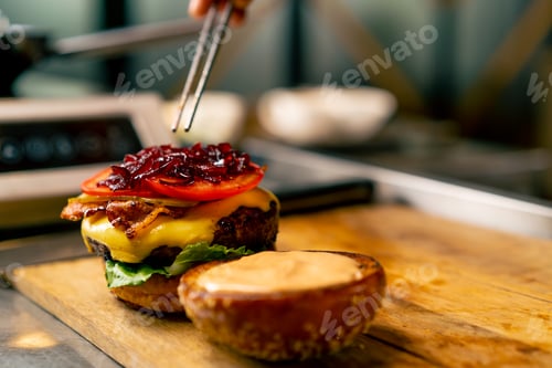 Preview: A close-up of chef preparing a burger with beef patty with vegetables and cheese in the kitchen