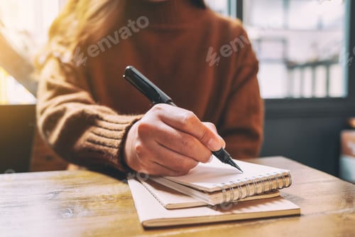 Preview: Closeup image of a woman writing on blank notebook with fountain pen on wooden table
