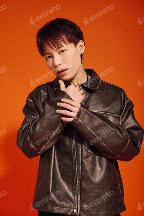Preview: Handsome stylish young asian man poses confidently against a vibrant orange backdrop