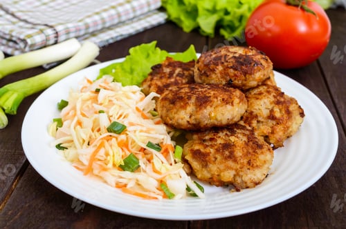 Preview: Juicy cutlets and salad with fresh vegetables: cabbage, carrots, greens on a white plate.
