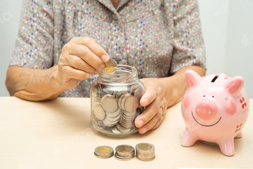 Preview: Asian elderly woman putting coin into pink piggy bank for saving money