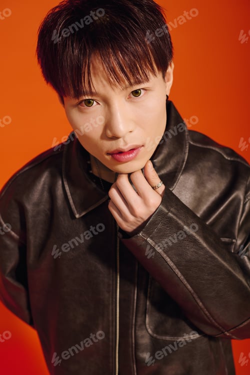 Preview: Stylish young Asian man posing confidently against a vibrant orange backdrop