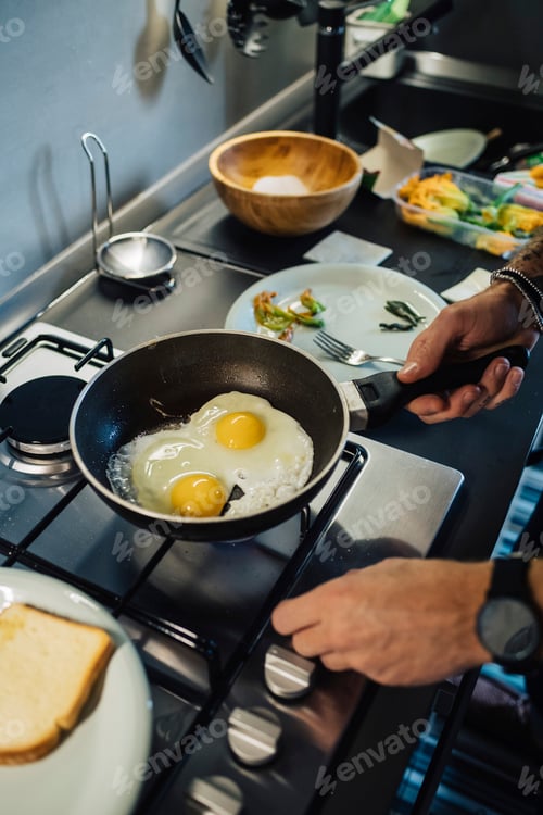 Preview: Mid adult man preparing fried eggs at kitchen hob, cropped close up