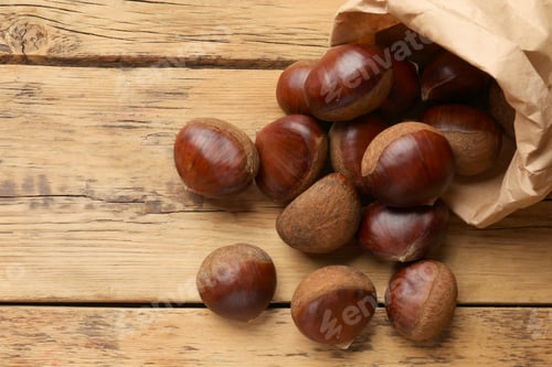 Preview: Sweet fresh edible chestnuts in paper bag on wooden table, top view. Space for text