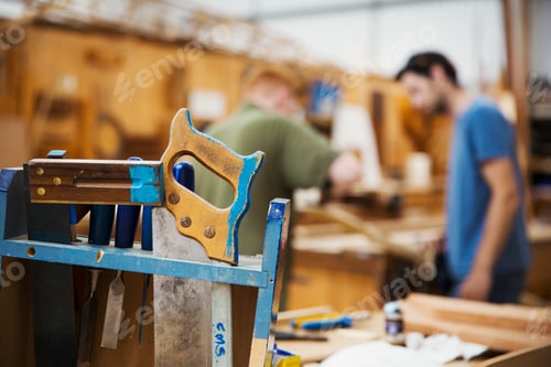 Preview: Close up of hand tools in boat-builder's workshop, two men working in background.