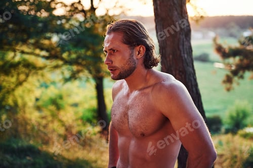Preview: Handsome shirtless man with muscular body type is in the forest at daytime