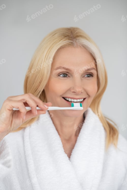 Preview: Smiling blonde woman brushing her teeth and looking happy