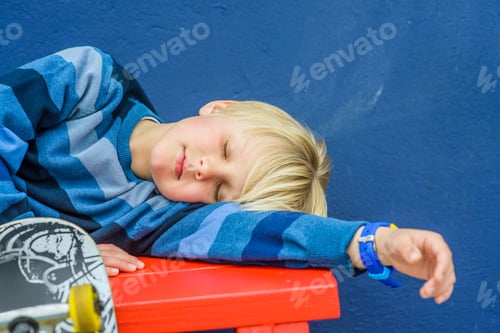 Preview: Boy with skateboard asleep on red bench
