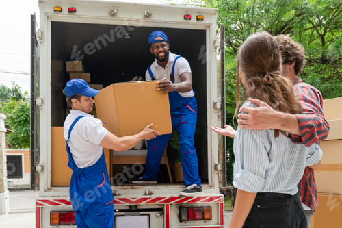 Preview: Two men movers in blue uniform lift cardboard box unloading from truck for moving house service