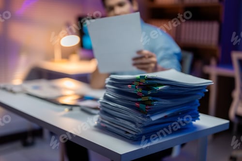 Preview: Office worker reviewing documents with a large stack of paperwork on desk