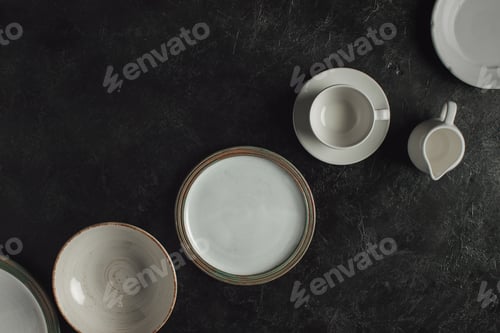 Preview: flat lay with ceramic plates, cup on saucer and jug isolated on black table