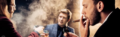 Preview: panoramic shot of handsome man smoking while playing poker on black with smoke