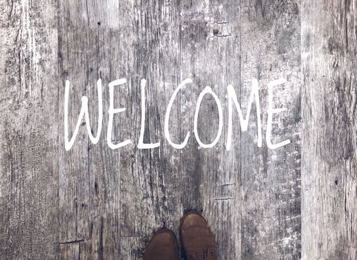 Preview: Top view of reclaimed wood floor with tips of shoes and a WELCOME sign