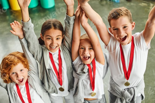 Preview: happy little boys and girls in sportswear with golden medals cheering and smiling at camera