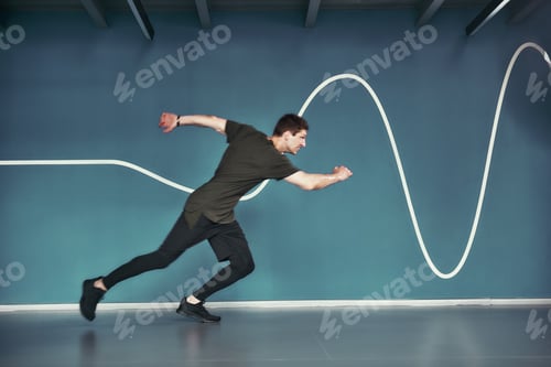 Preview: Great shape. Full length of young athletic man in sport clothing running against blue wall while