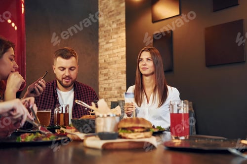 Preview: By the table. Group of young friends sitting together in bar with beer