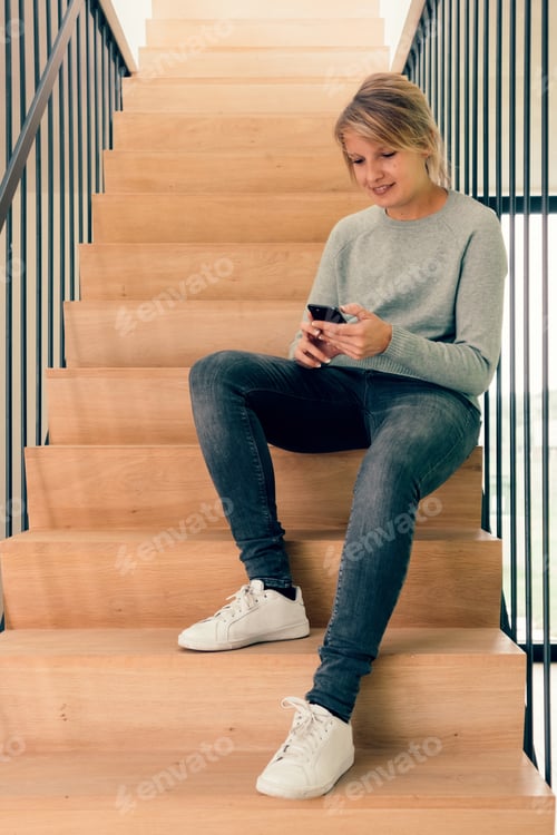 Preview: Girl at home using phone app sitting on the stairs