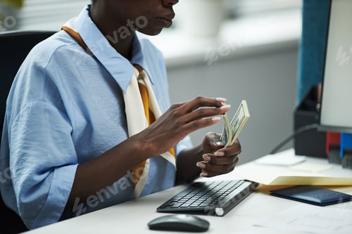 Preview: Young Black Woman Counting Cash at Desk in Bank Office Environment
