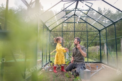 Preview: Father learning his little daughter to care about organic plants in eco greenhouse, sustainable