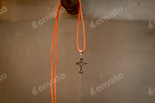 Preview: Silver orthodox cross on orange cord hanging in front of church interior background