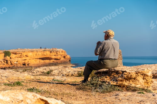 Preview: Pensive old man sitting on the shoreline by the sea. Traditional lord of Spanish culture
