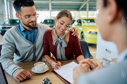 Preview: Happy woman and her husband signing agreement during a meeting with car salesperson in showroom.