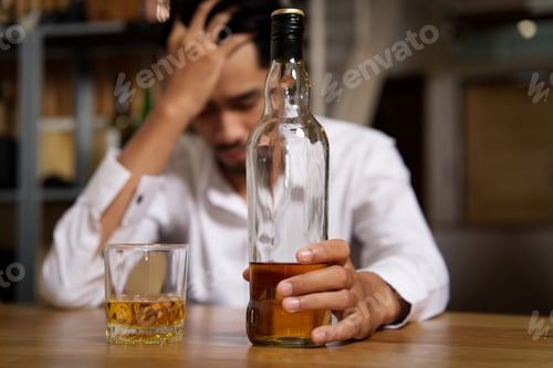 Preview: Drunk man sitting at the bar in pub and holding whisky bottle in left hand.