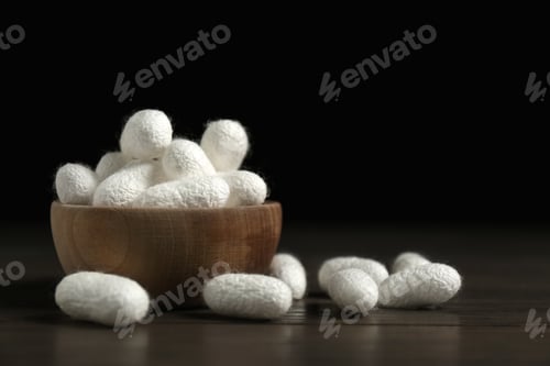 Preview: White silk cocoons with bowl on wooden table, closeup. Space for text