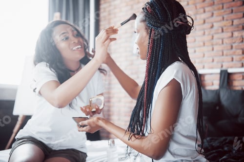 Preview: Two beautiful african girl in sleepwear smiling sitting on bed at home woke up in the morning