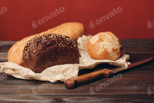 Preview: loaf of rye bread and flour products on paper packaging knife on a wooden table and red background