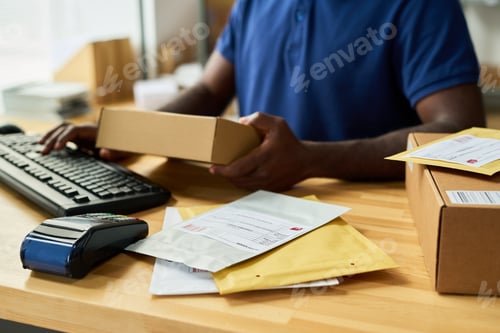 Preview: Young Adult Black Man Processing Parcels at Counter Using Computer Keyboard