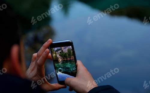 Preview: Closeup of a man taking a picture of the lake with his phone