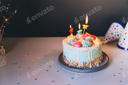 Preview: Colorful birthday cake with sprinkles and burning star shaped candles on a dark wall background.