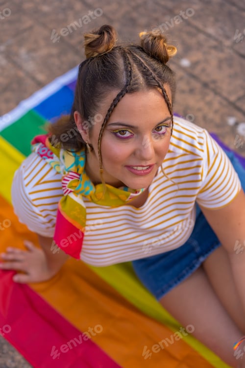 Preview: A vertical shot of a young Caucasian female sitting on LGBT pride flag outdoors