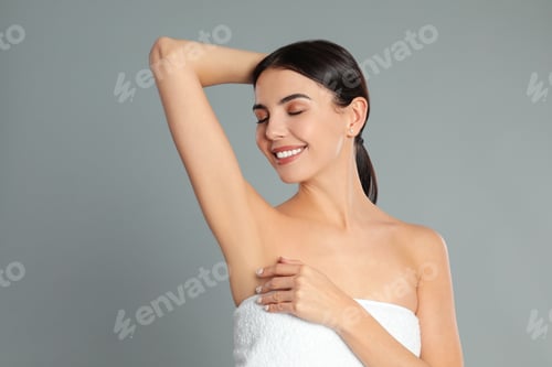 Preview: Young woman showing hairless armpit after epilation procedure on grey background