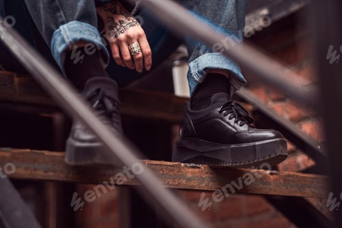 Preview: Close-up photo of fashionable female legs in boots sitting on stairs outside.