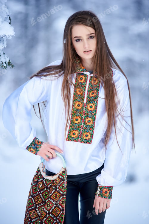 Vista previa: Young woman in jeans and white traditional embroidered blouse with linen bag on winter background.