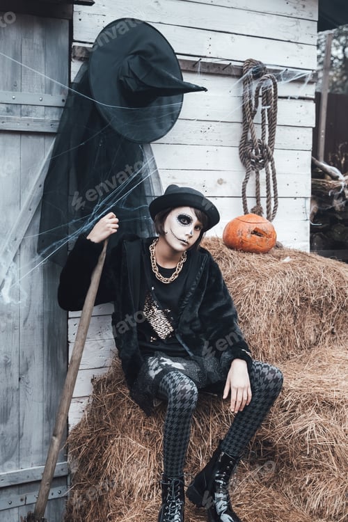 Preview: Beautiful scary little girl celebrating halloween. Terrifying black, white half-face makeup,witch co