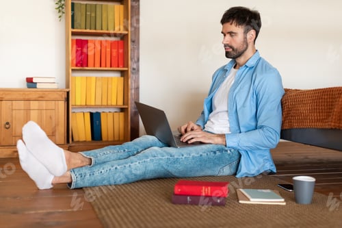 Preview: Young Man Working on Laptop While Sitting on Wooden Floor