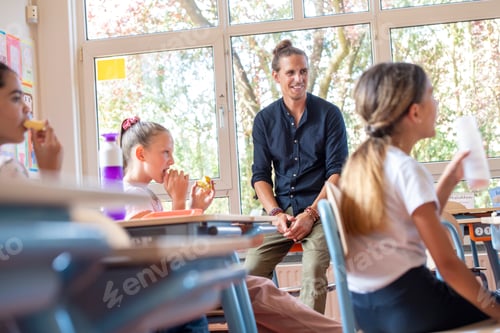 Visualização: Professor masculino sentado com seus alunos na sala de aula no intervalo enquanto eles almoçam