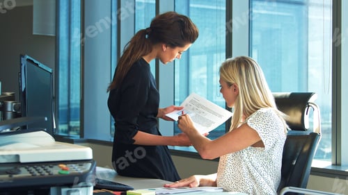Preview: Two Female Business Colleagues Sitting At Desk In Office Discussing Documents