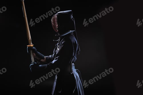 Preview: Side view of kendo fighter in traditional helmet holding bamboo sword on black