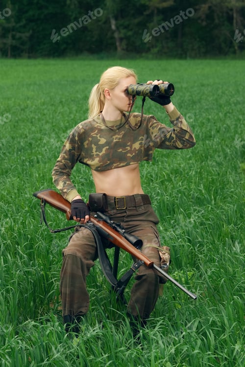 Preview: Attractive hunter girl with hunting carbine looking into binoculars.