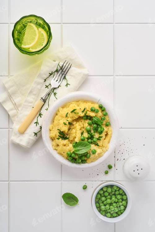 Preview: Mashed potato with butter, green peas, onions, basil on white ceramic tile background. Top view with