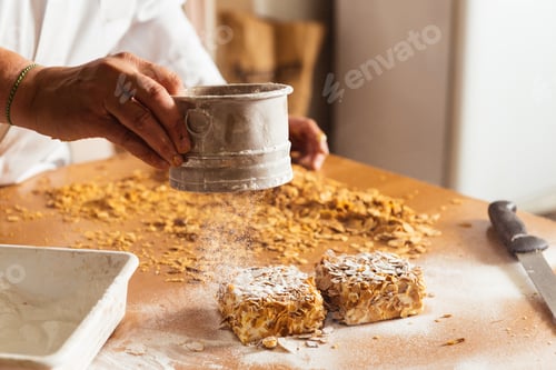 Preview: Unrecognizable man holding metal measure and sprinkling sugar powder on small cakes