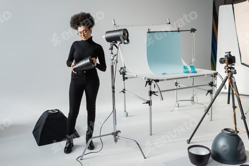 Preview: full length of african american content producer holding part of strobe lamp while working with