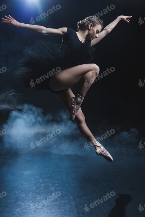 Preview: attractive elegant ballet dancer in pointe shoes and black tutu in studio with smoke