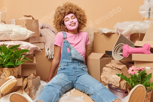 Preview: Indoor shot of positive curly haired undergoes beauty procedures dressed in t shirt denim overalls p